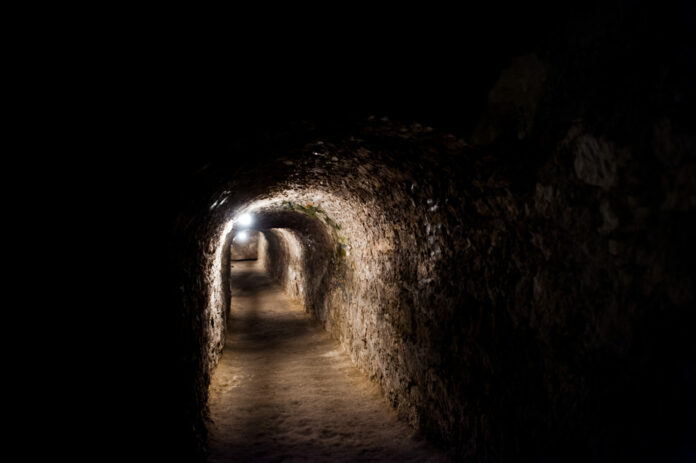 Dark scarry tunnel with a few lights under the castle.